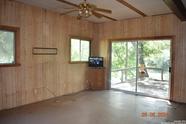 unfurnished room featuring beamed ceiling, a healthy amount of sunlight, ceiling fan, and wooden walls