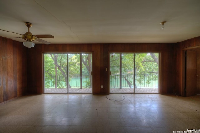 spare room with wood walls, a ceiling fan, and a healthy amount of sunlight