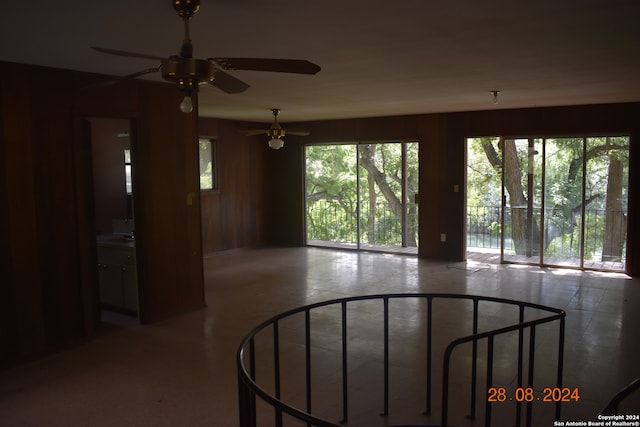 interior space with ceiling fan, wood walls, and concrete flooring