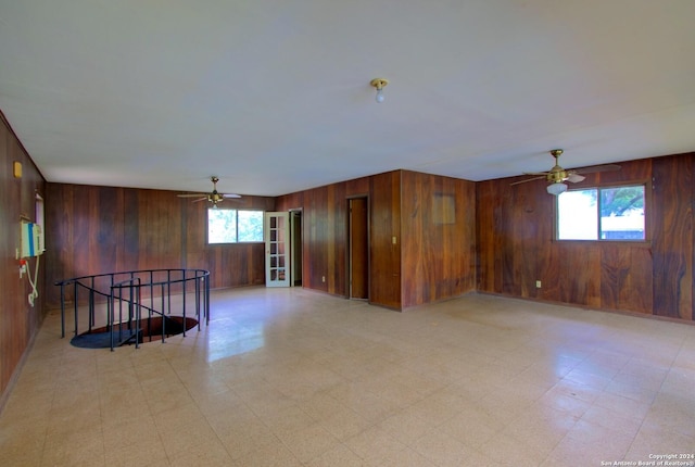 unfurnished room with light floors, wood walls, and ceiling fan