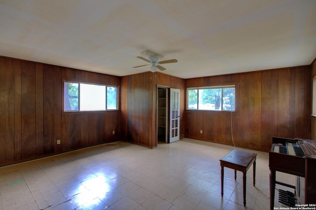 empty room with light floors, a healthy amount of sunlight, ceiling fan, and wooden walls