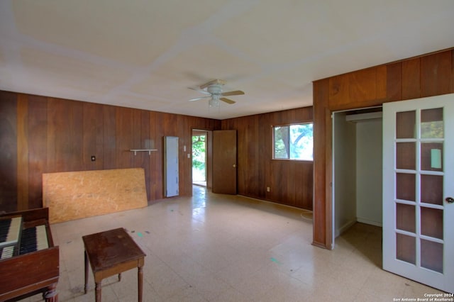 living room with a ceiling fan, wooden walls, and light floors