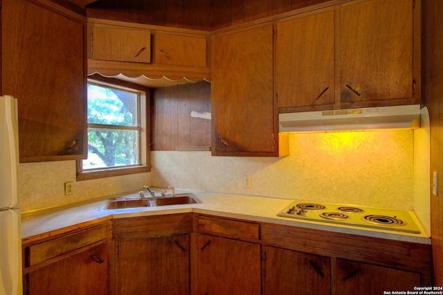 kitchen with white appliances, brown cabinetry, a sink, light countertops, and under cabinet range hood