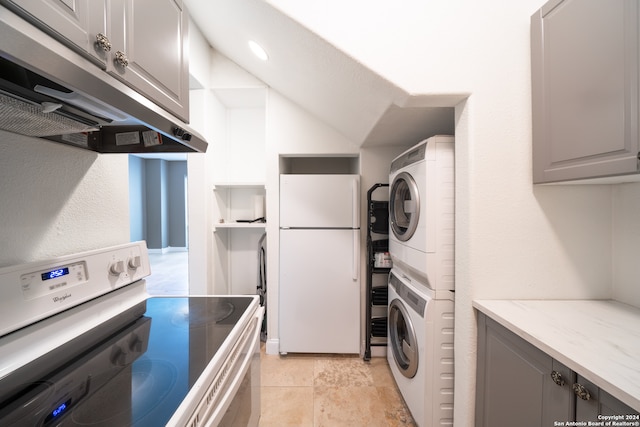 kitchen with stove, stacked washing maching and dryer, gray cabinetry, light tile patterned floors, and white refrigerator