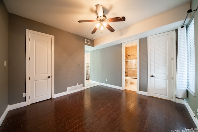 unfurnished bedroom featuring connected bathroom, ceiling fan, dark hardwood / wood-style flooring, and multiple windows