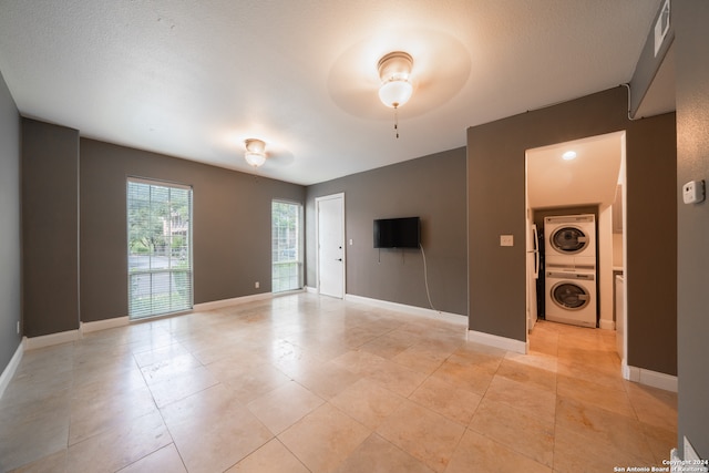 empty room with a textured ceiling, ceiling fan, and stacked washer and clothes dryer