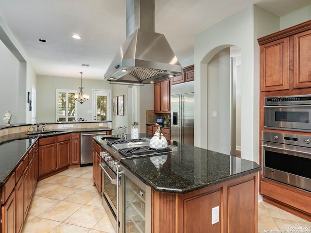 kitchen featuring dark stone countertops, a center island, a chandelier, premium appliances, and island range hood