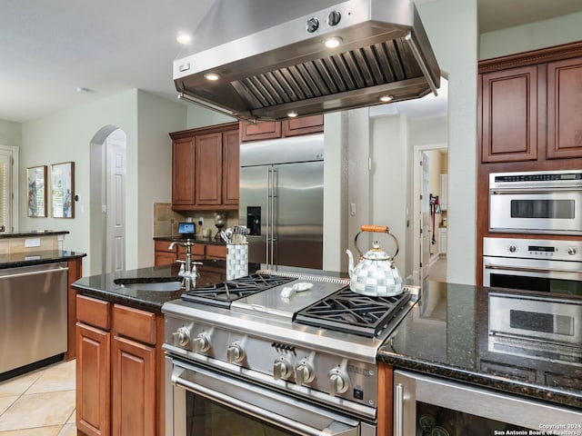 kitchen with dark stone countertops, island range hood, high quality appliances, and sink