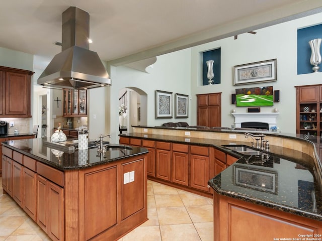 kitchen with a kitchen island with sink, dark stone counters, light tile patterned floors, sink, and island exhaust hood