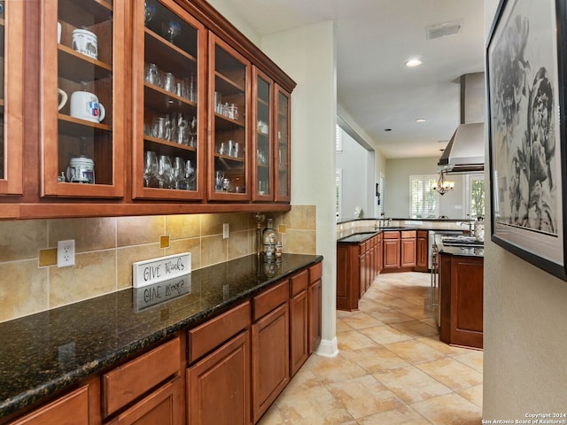 kitchen with an inviting chandelier, tasteful backsplash, island exhaust hood, sink, and dark stone counters