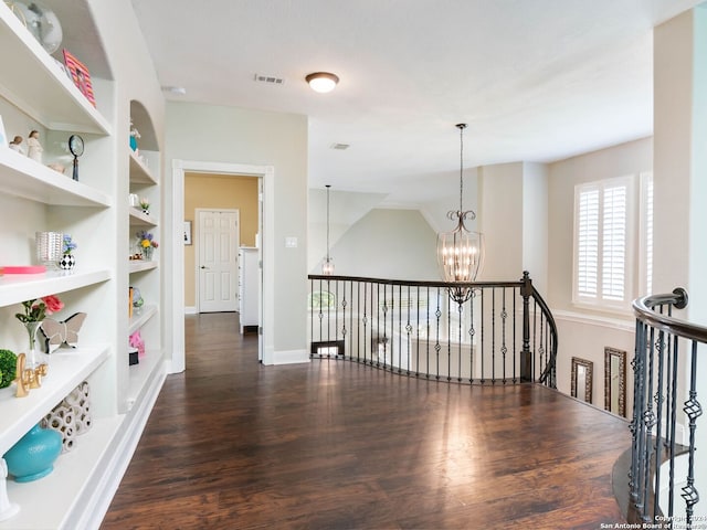 hallway with dark wood-type flooring, built in features, and an inviting chandelier