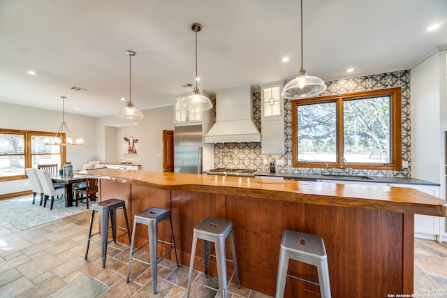 kitchen featuring a kitchen breakfast bar, decorative light fixtures, wood counters, sink, and custom exhaust hood