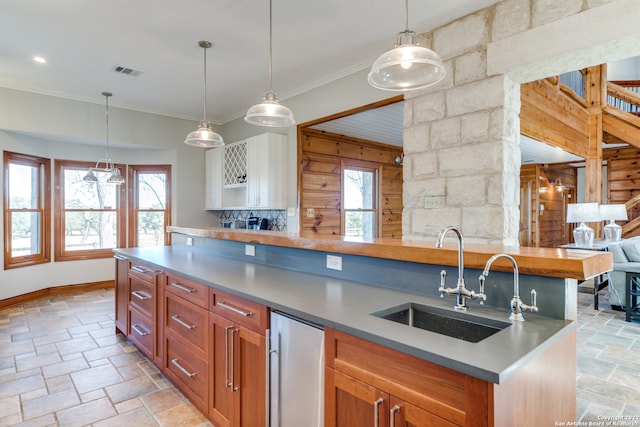 kitchen with a center island with sink, pendant lighting, ornamental molding, and sink