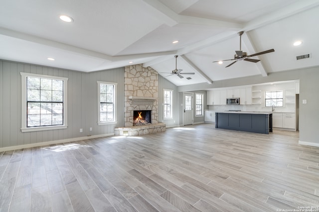 unfurnished living room featuring ceiling fan, a fireplace, vaulted ceiling with beams, and light hardwood / wood-style flooring