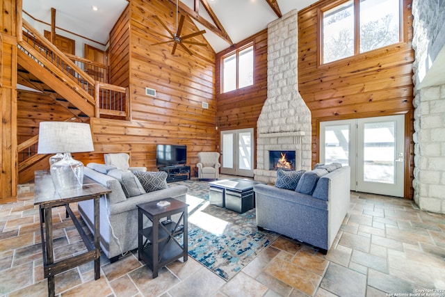 living room with a fireplace, beamed ceiling, high vaulted ceiling, wood walls, and ceiling fan