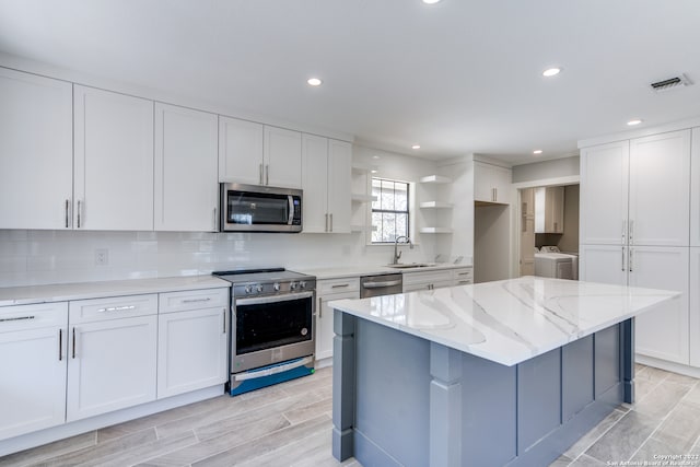 kitchen with white cabinetry, washer and dryer, stainless steel appliances, light stone counters, and sink