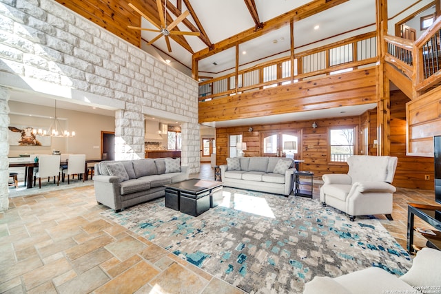 living room featuring wood walls, ceiling fan with notable chandelier, beamed ceiling, and a towering ceiling