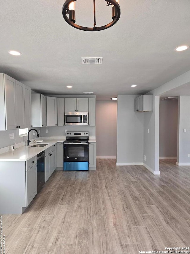 kitchen featuring a textured ceiling, stainless steel appliances, sink, gray cabinets, and light wood-type flooring