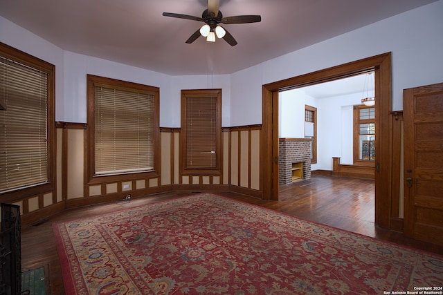 unfurnished room with ceiling fan, a brick fireplace, and dark hardwood / wood-style flooring