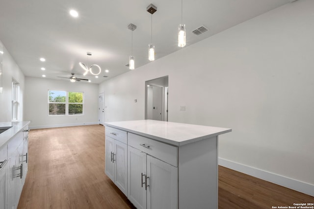 kitchen featuring hanging light fixtures, ceiling fan with notable chandelier, a center island, and light hardwood / wood-style floors