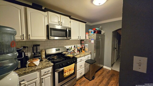 kitchen with white cabinets, crown molding, appliances with stainless steel finishes, dark hardwood / wood-style floors, and dark stone counters