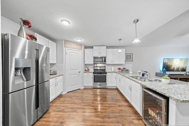 kitchen featuring beverage cooler, appliances with stainless steel finishes, hanging light fixtures, kitchen peninsula, and sink