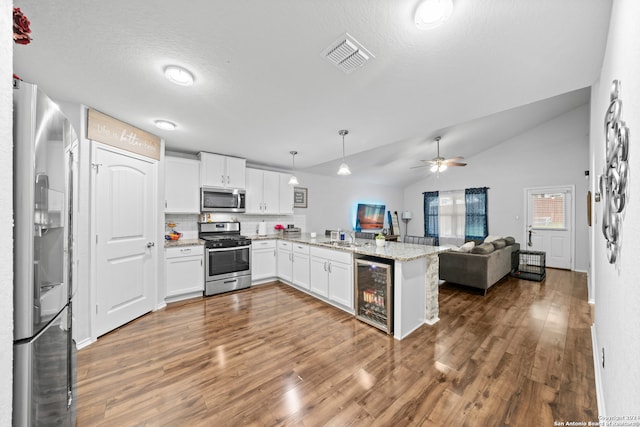 kitchen with decorative light fixtures, appliances with stainless steel finishes, lofted ceiling, kitchen peninsula, and beverage cooler