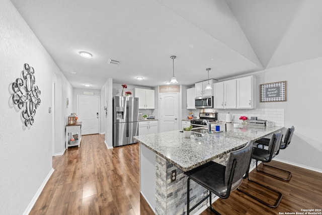 kitchen featuring tasteful backsplash, kitchen peninsula, a breakfast bar, appliances with stainless steel finishes, and hardwood / wood-style flooring