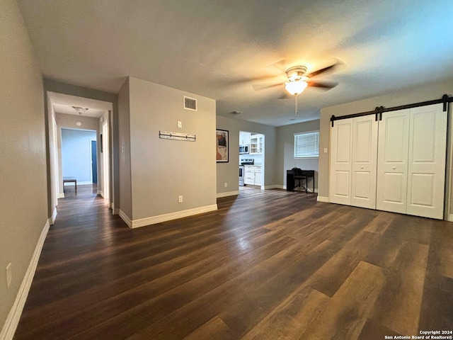 interior space featuring dark wood-type flooring, ceiling fan, and a barn door