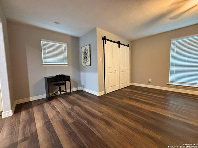 unfurnished bedroom with a barn door, multiple windows, dark hardwood / wood-style floors, and a closet