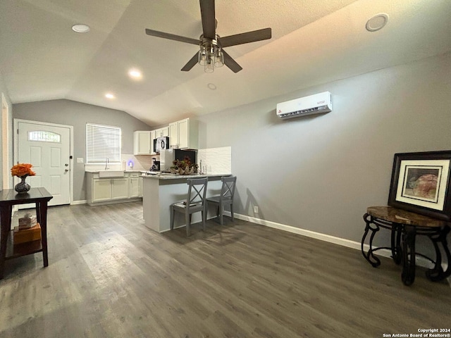 interior space with vaulted ceiling, a wall mounted air conditioner, dark wood-type flooring, sink, and ceiling fan