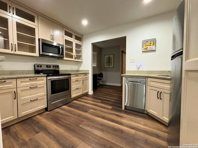 kitchen with light stone counters, stainless steel appliances, dark hardwood / wood-style floors, and cream cabinetry