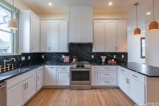 kitchen with white cabinets, appliances with stainless steel finishes, a peninsula, light wood-type flooring, and a sink