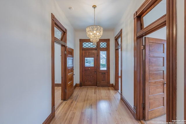 foyer entrance with light wood-type flooring, a notable chandelier, and baseboards