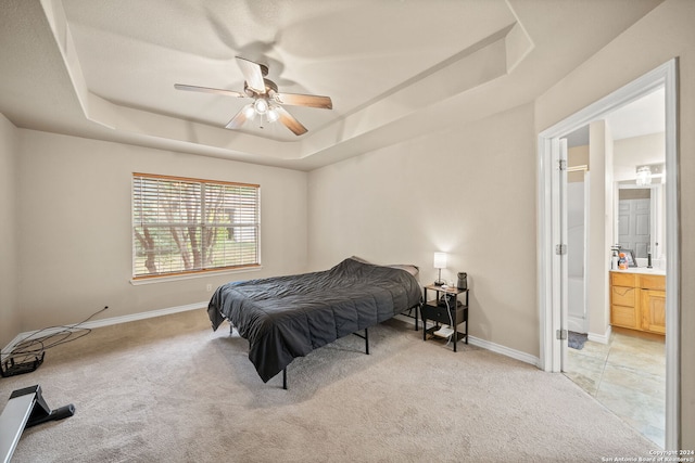 bedroom featuring ceiling fan, ensuite bathroom, and a tray ceiling