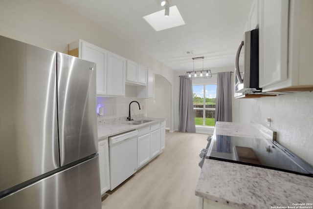 kitchen with a skylight, light hardwood / wood-style flooring, stainless steel appliances, sink, and white cabinets