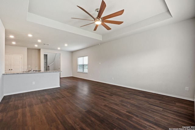 unfurnished living room featuring dark wood-type flooring, ceiling fan, and a tray ceiling