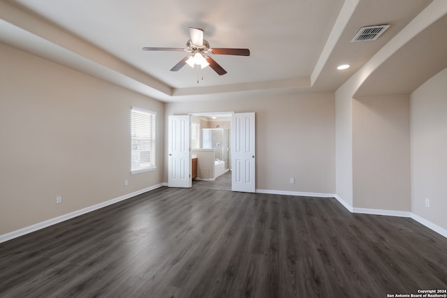 unfurnished bedroom with dark wood-type flooring, connected bathroom, a raised ceiling, and ceiling fan