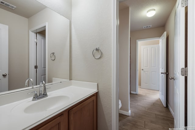 bathroom featuring hardwood / wood-style floors, toilet, a textured ceiling, and vanity