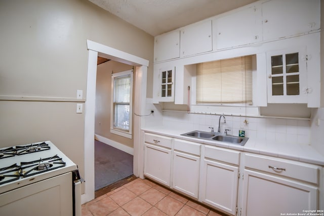 kitchen featuring light tile patterned floors, tasteful backsplash, white gas range, sink, and white cabinetry