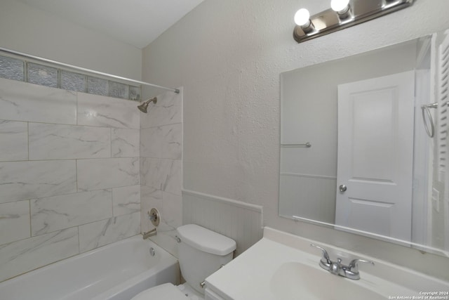 bathroom with shower / bath combination, a textured wall, toilet, wainscoting, and vanity