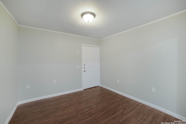 empty room with crown molding, dark wood finished floors, and baseboards