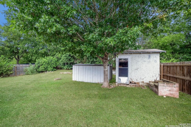 view of yard with a fenced backyard, a storage unit, and an outbuilding