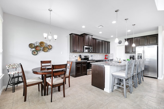 kitchen featuring an inviting chandelier, light stone countertops, stainless steel appliances, a kitchen island with sink, and tasteful backsplash