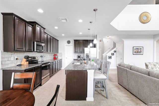 kitchen with decorative light fixtures, light stone countertops, appliances with stainless steel finishes, an island with sink, and decorative backsplash