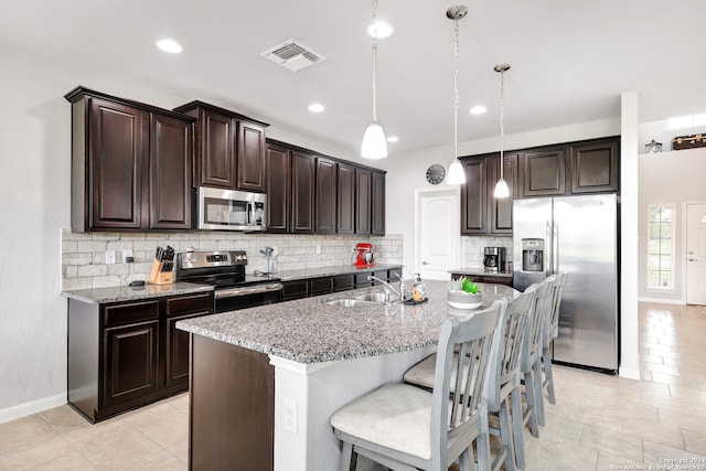 kitchen featuring decorative light fixtures, stainless steel appliances, a kitchen breakfast bar, and a center island with sink