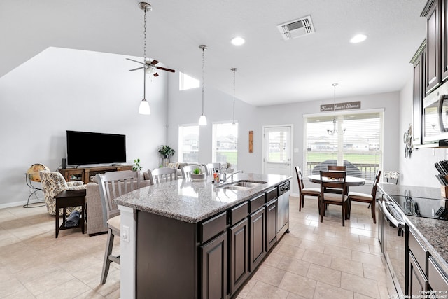 kitchen featuring ceiling fan with notable chandelier, light stone countertops, an island with sink, stainless steel appliances, and sink