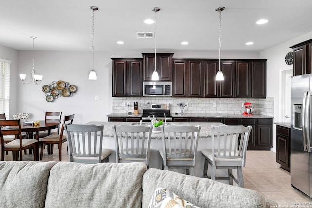 kitchen with hanging light fixtures, light tile patterned floors, appliances with stainless steel finishes, dark brown cabinets, and a breakfast bar