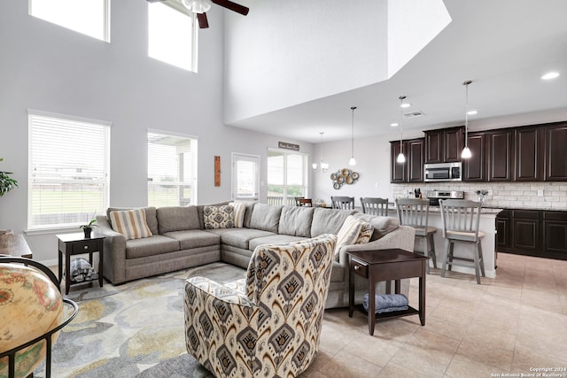 living room with a towering ceiling, a wealth of natural light, light tile patterned floors, and ceiling fan