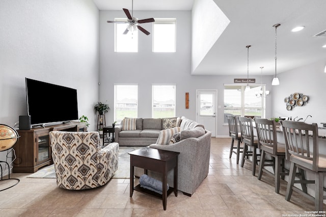 tiled living room featuring ceiling fan with notable chandelier and a high ceiling